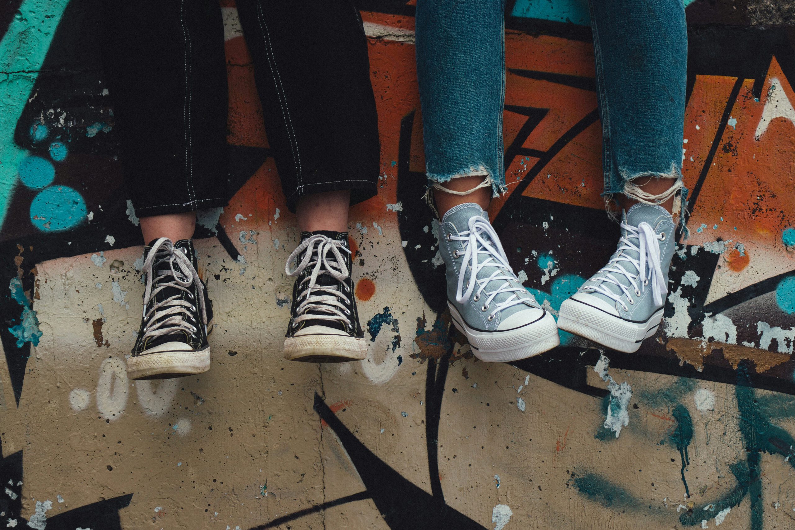 Zu sehen sind Unterschenkel und Füße mit Turnschuhen vor eine mit Graffiti besprühten Wand.