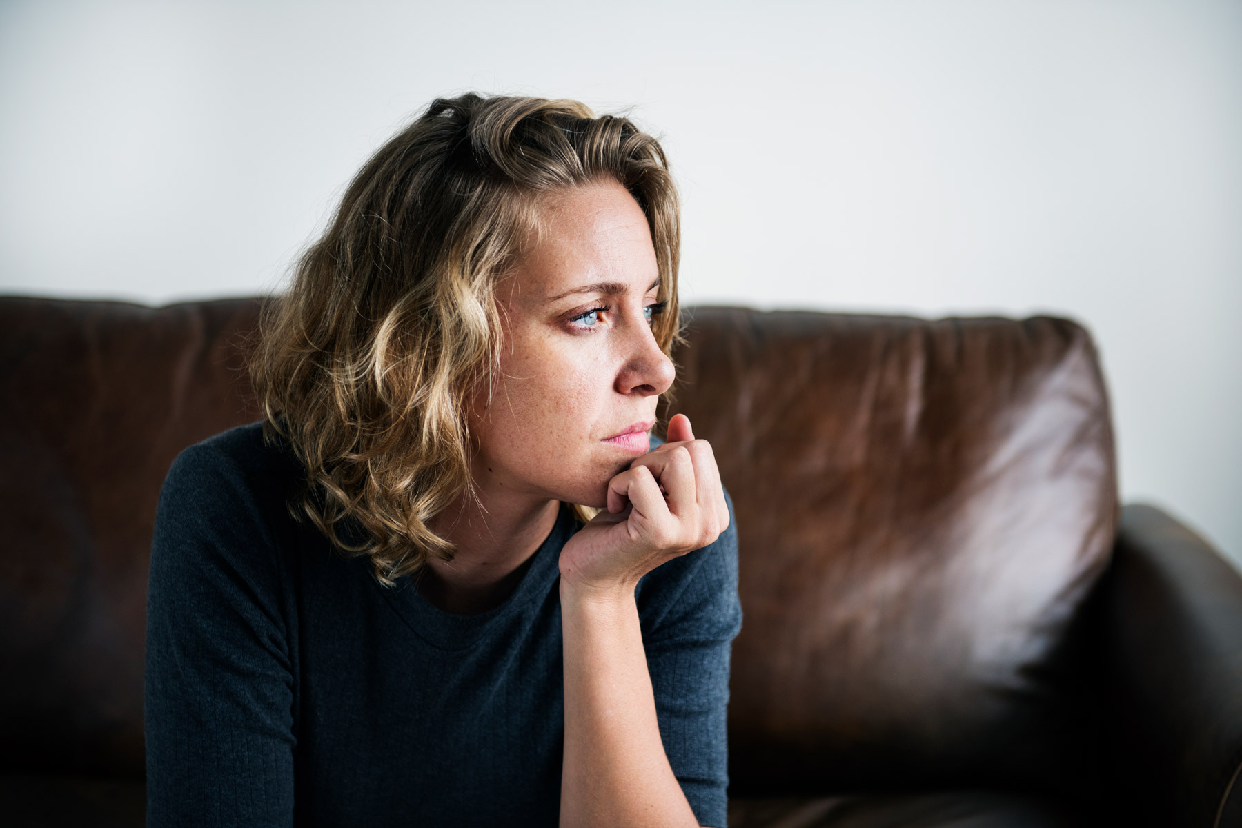 Eine Frau sitzt auf dem Sofa. Sie schaut zur Seite und sieht nachdenklich und verzweifelt aus.