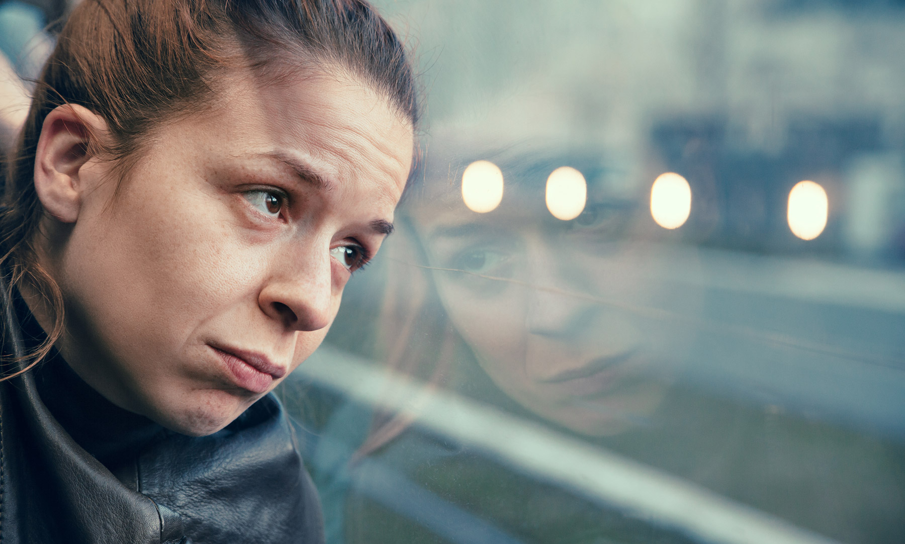 Eine Frau sitz im Zug und hat ihren Kopf an die Glasscheibe gelehnt. Sie sieht unglücklich aus.