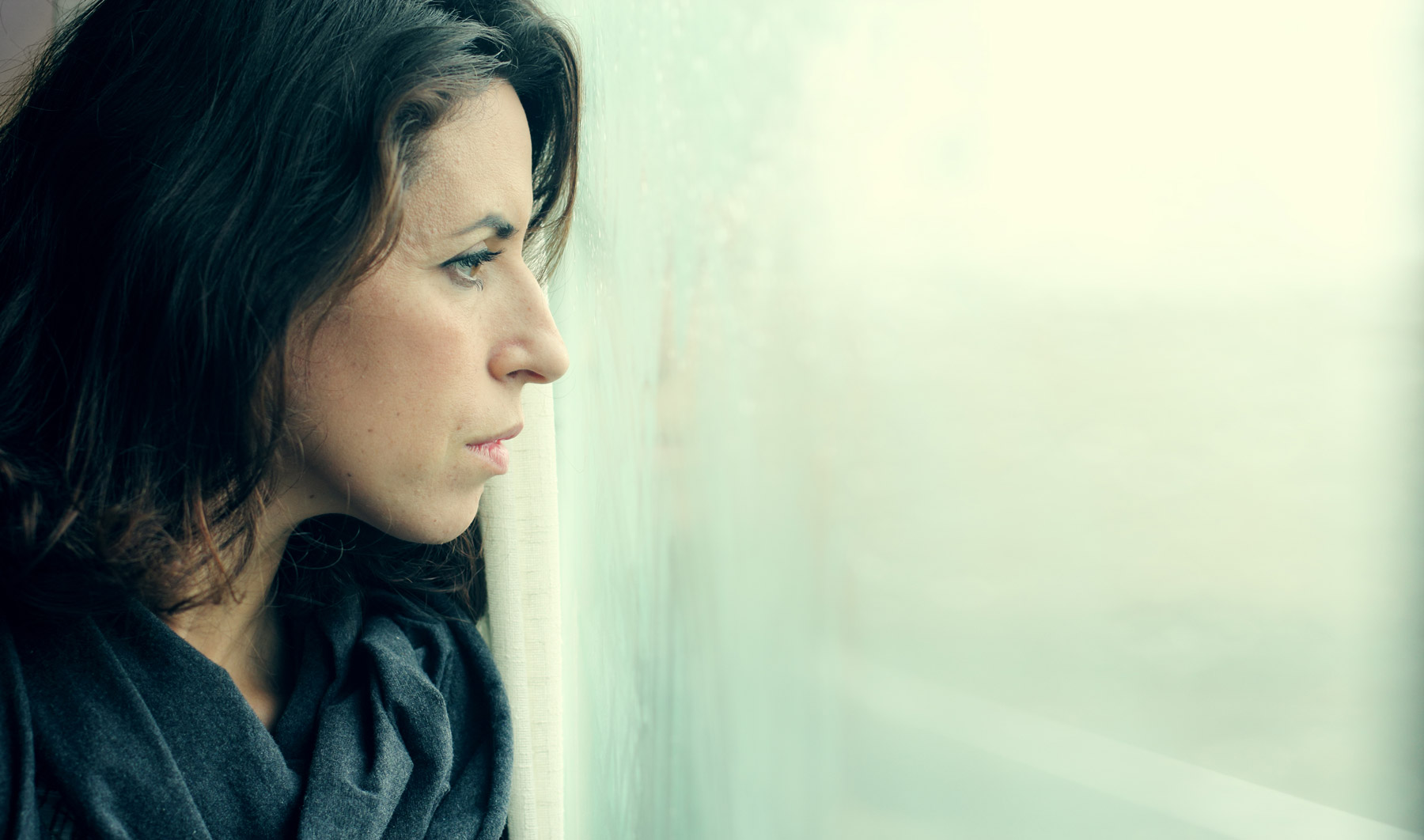 Eine Frau im Profil. Sie schaut nachdenklich aus dem Fenster. Das Bild wirkt trostlos.