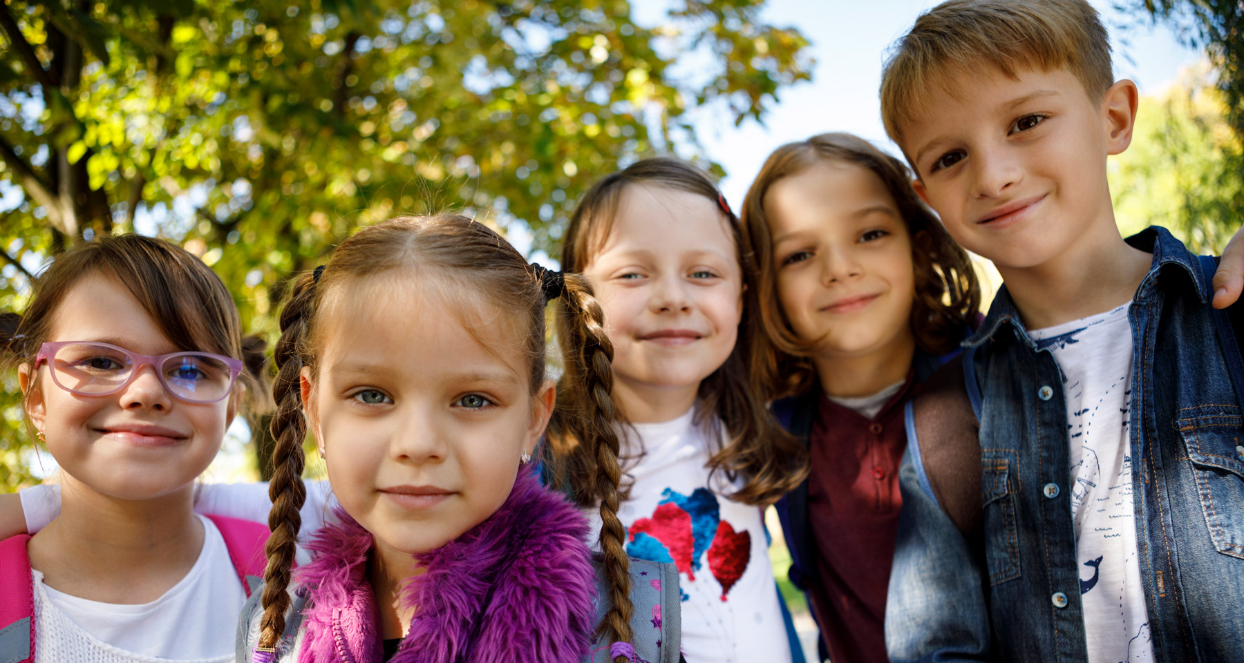 Fünf Kinder stehen nebeneinander und lachen. Das Bild ist farbenfroh und freundlich.