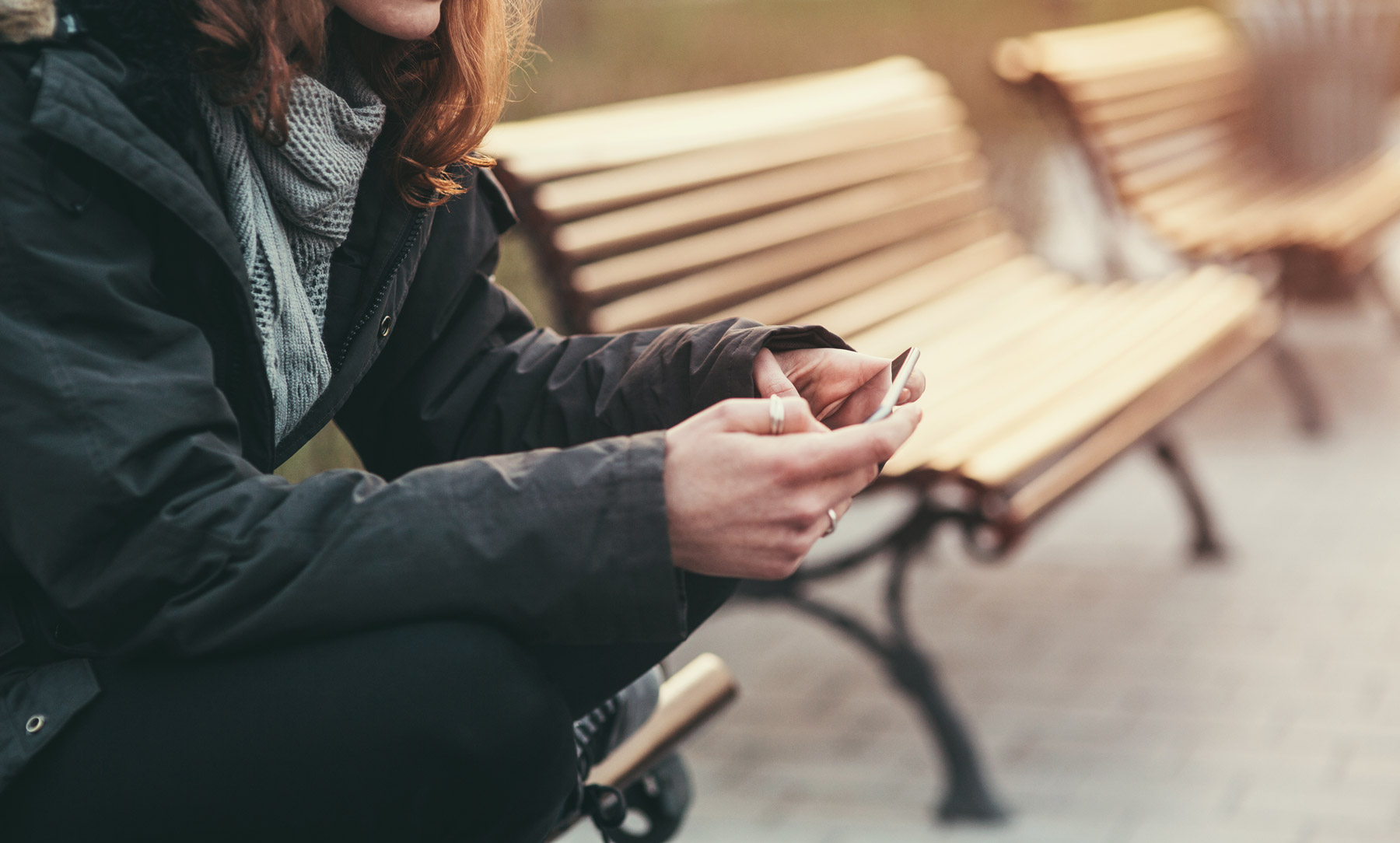 EineFrau sitzt auf einer Bank und hält ihr Smartphone in der Hand. Ihr Gesicht ist nicht auf dem Bild zu sehen.