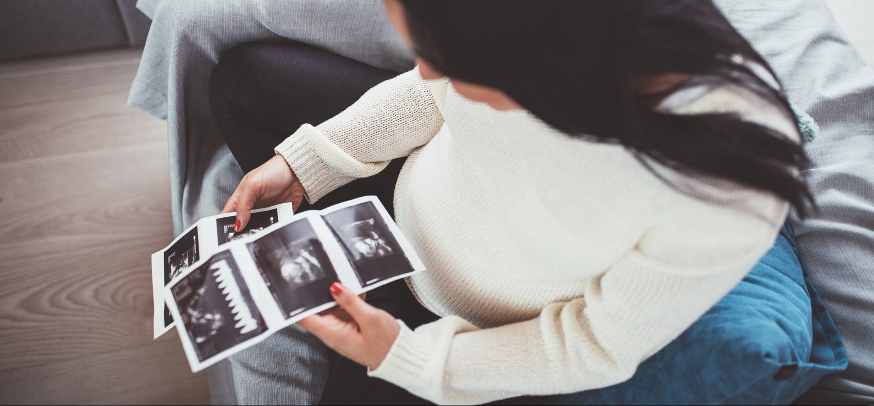 Eine Frau schräg von oben fotografiert mit Ultraschallbildern in der Hand.