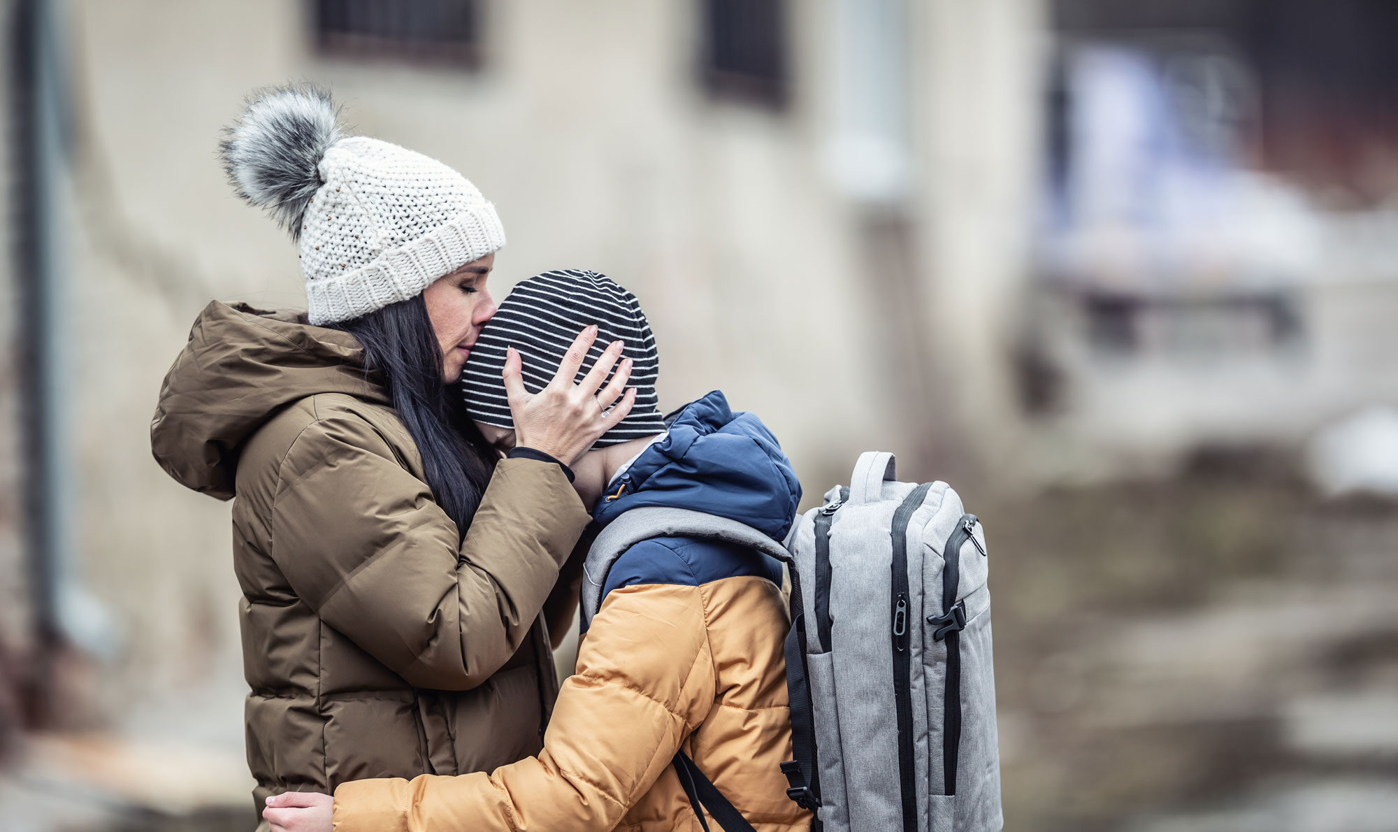 Eine Frau küsst ihren Sohn auf den Kopf. Sie sind warm gekleidet und sehen verzweifelt bzw. unglücklich aus.
